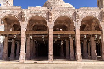 Fototapeta premium Covered courtyard of Al Sahaba Mosque in Sharm El Sheikh Egypt featuring ornate stone arches Islamic carvings and traditional hanging lanterns beneath a clear blue sky