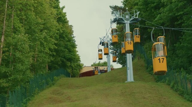 Yellow cable car moving in park. Tourists riding ropeway lift for sightseeing outdoor view. Transportation system over green hill for fun activity in summer day.