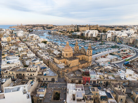 Aerial view of the Basilica of Saint Joseph and the marina filled with boats surrounded by dense urban architecture in Msida, Eastern Region, Malta.