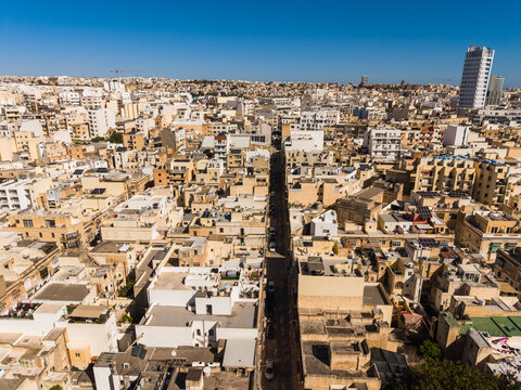 Aerial view of the dense urban landscape with traditional limestone buildings, flat rooftops, and a narrow street under a clear blue sky in Msida, Eastern Region, Malta.