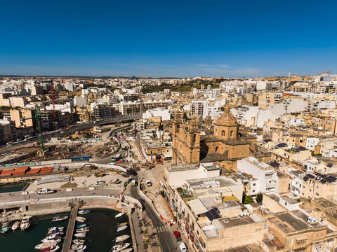 Aerial view of Saint Joseph Parish Church and the harbor with boats surrounded by dense urban architecture and construction sites in Msida, Eastern Region, Malta.