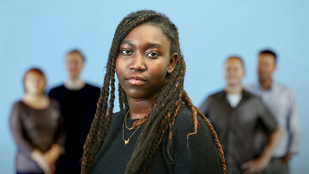 Confident young Black businesswoman leading a diverse corporate team against a blue background
