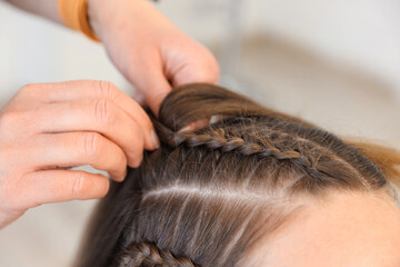 Fototapeta premium Hairstylist braiding teenage girl's hair indoors, closeup
