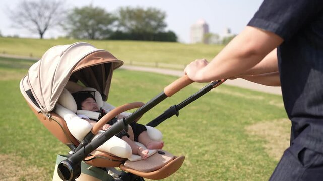 Soft canopy shields a sleeping infant. Parent gently pushes stroller through grassy park. Sunlight warms green fields behind. Scene captures calm, nurturing moment. Ideal for parenting, family