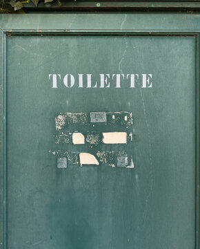 Vintage green toilette sign on weathered restroom door