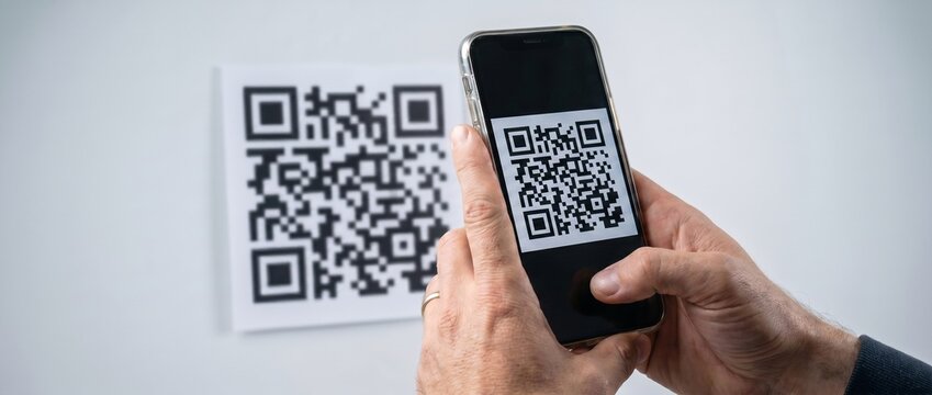  Close-up of male hands holding a smartphone and scanning a QR code on a white wall. Contactless digital technology and mobile payment concept