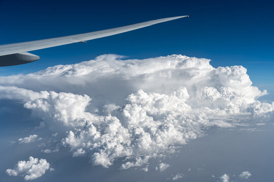Aerial view of an airplane wing over massive white cumulus clouds and a deep blue sky in India.