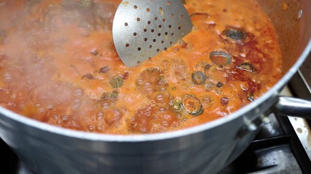 Professional chef preparing a traditional seafood dish. Limpets boiling in a large pot with a rich and steaming tomato sauce, slowly stirred