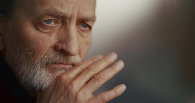 Close-up portrait of contemplative elderly man gray beard and hand near mouth