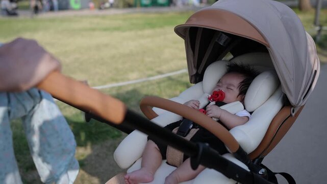 Soft canopy shields a sleeping infant. Baby holds a red pacifier, eyes closed. Hands guide the stroller gently forward. Peaceful stroll through a park setting. Ideal for parenting, baby