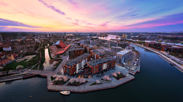 Aerial view of the Museum of the Second World War and modern buildings along the Motlawa River under a vibrant sunset sky in Gdansk, Pomeranian Voivodeship, Poland.