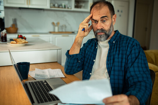 Concerned middle-aged man reviewing bills at home kitchen table