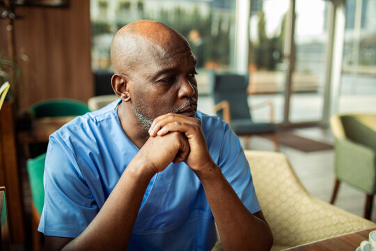 Thoughtful healthcare worker in blue scrubs at cafe