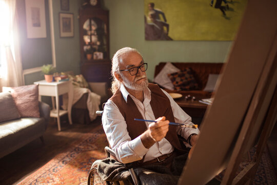Senior man in wheelchair painting in home studio
