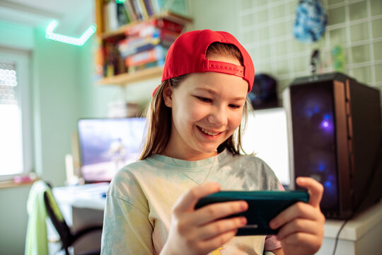 Smiling tween girl gaming on smartphone in home bedroom