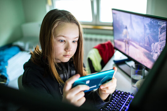 Teen girl playing mobile game at home computer desk