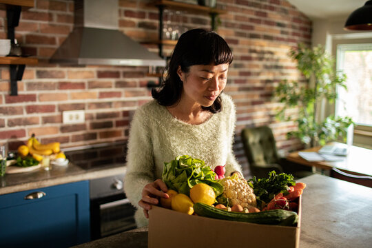 Woman unpacking organic vegetable delivery at home kitchen