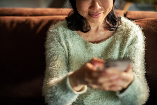 Woman using smartphone on cozy sofa at home