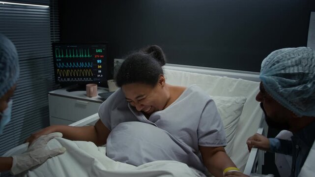 Pregnant Black woman pushing during childbirth in hospital bed with husband and doctor assisting. Footage is perfect for maternity care and medical services advertising
