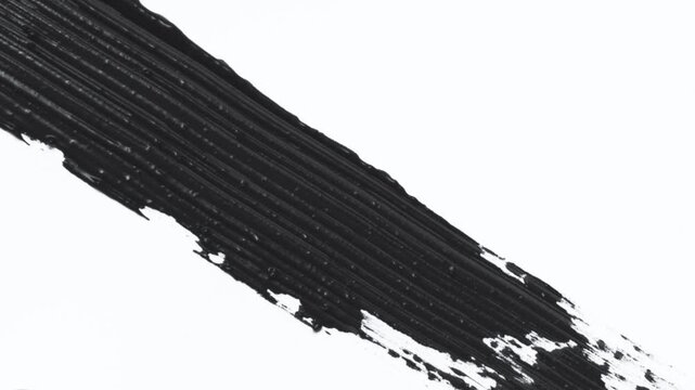 Close up of black mascara brush strokes on white background. Macro shot of wand with mascara texture smudge swatch