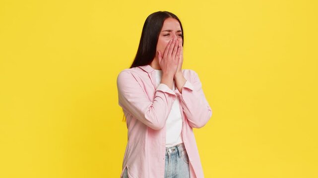 Young woman rubbing eyes with tired exhausted expression, showing signs of overwork and strong need for rest. Girl on yellow background visibly demonstrates fatigue, sleepiness, and physical depletion