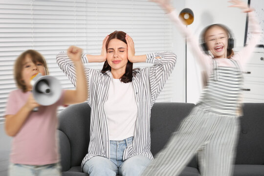 Family with hyperactive children. Tired mother suffering from headache on sofa while her kids having fun