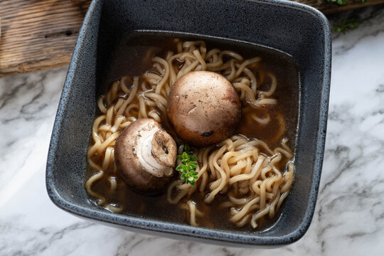 Korean style mushroom and noodles soup or pho, garnished with fresh thyme, in a black square bowl on a marbled background.