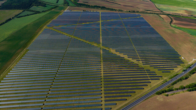 Aerial view of the Veprek Solar Park with vast rows of solar panels surrounded by green agricultural fields and a rural road in Nova Ves u Melnika, Central Bohemian Region, Czechia.