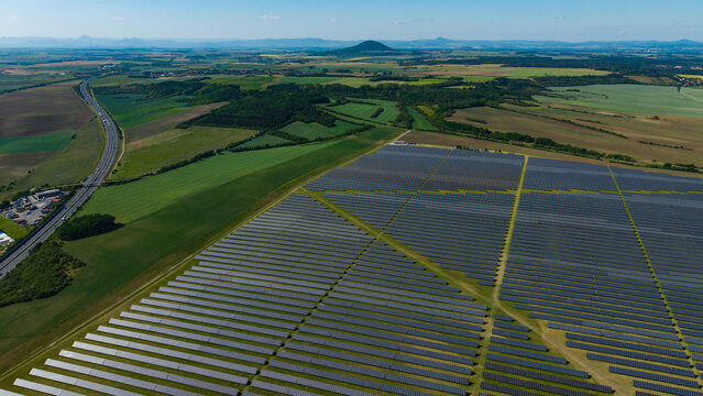 Aerial view of Veprek Solar Park with rows of photovoltaic panels surrounded by green fields and a highway in Nova Ves u Melnika, Central Bohemian Region, Czechia.