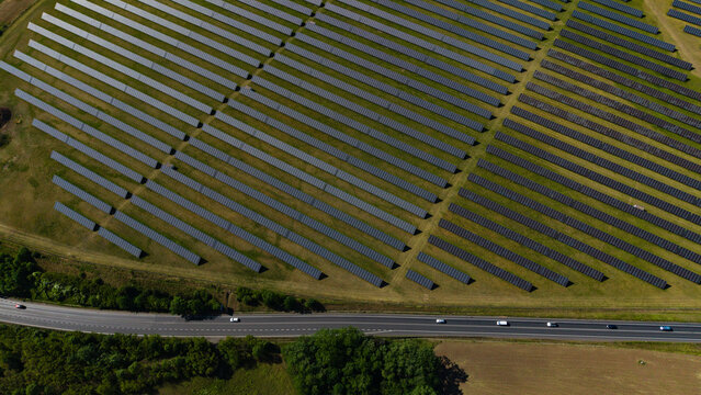 Aerial view of Veprek Solar Park with rows of photovoltaic panels on green fields next to a highway with cars in Nova Ves u Melnika, Central Bohemian Region, Czechia.