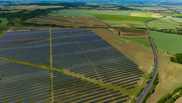 Aerial view of Veprek Solar Park with rows of photovoltaic panels surrounded by green agricultural fields and a winding road Nova Ves u Melnika, Central Bohemian Region, Czechia.