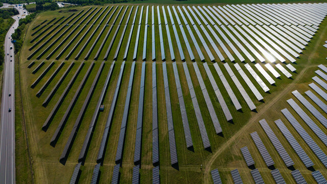 Aerial view of rows of photovoltaic panels at Veprek Solar Park with a highway and lush green fields Nova Ves u Melnika, Central Bohemian Region, Czechia.