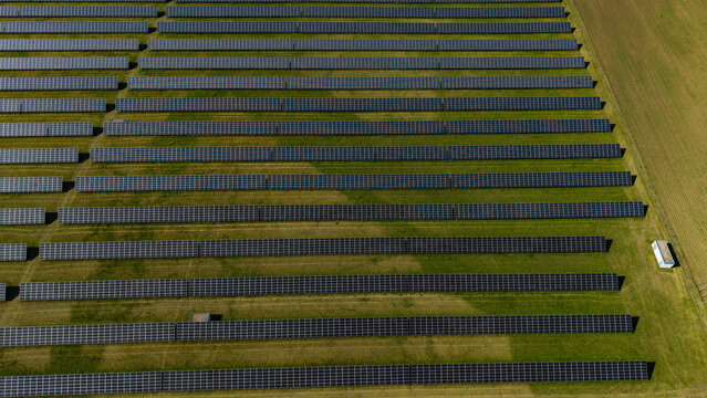 Aerial view of rows of solar panels at Veprek Solar Park surrounded by green fields in Nova Ves u Melnika, Central Bohemian Region, Czechia.