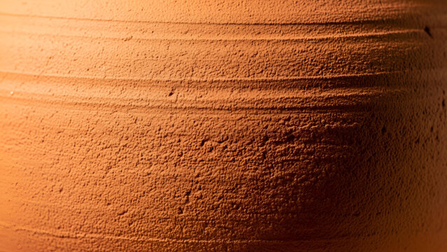 Close-up of a textured, orange terracotta pot with horizontal lines and rough surface details in warm lighting conditions