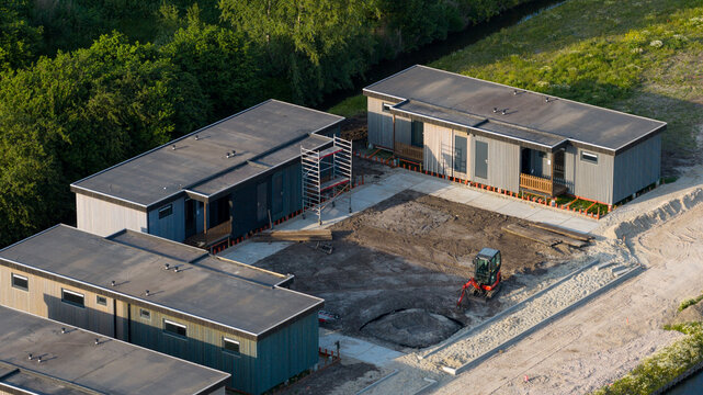 Aerial view of modern modular houses under construction with a small excavator and scaffolding in a residential development Ter Aar, Zuid-Holland, Netherlands.