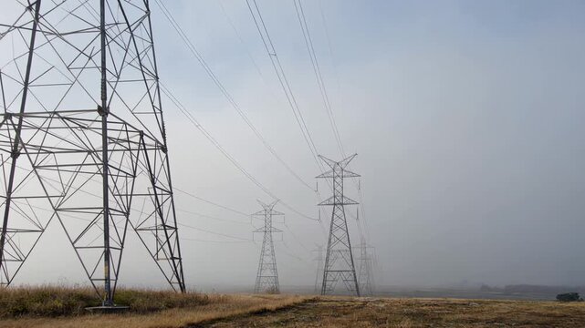 Dramatic low angle shot of high voltage power pylons stretching into a thick foggy sky