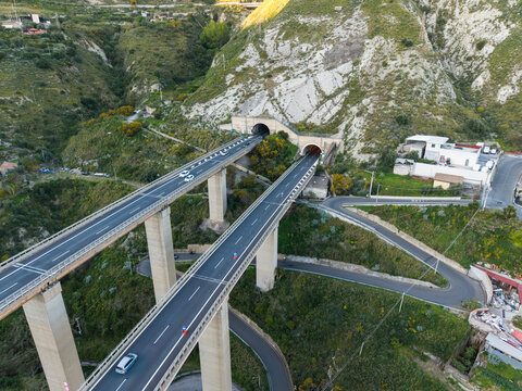 Aerial view of a modern highway viaduct with parallel bridges leading into mountain tunnels through a rocky green landscape Taormina, Sicily, Italy.