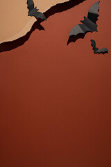 Fototapeta premium Happy Halloween paper bat decorations on torn brown and orange background with vertical strong shadows