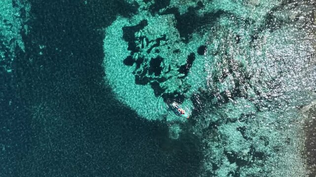 Drone shot of transparent blue ocean water with rocky reef texture and surf board 