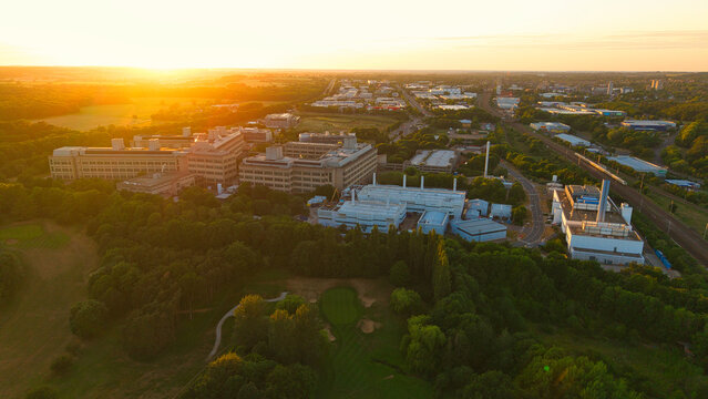 Aerial view of the GSK Stevenage research campus during a golden hour sunset with lush green trees and the urban skyline in the distance Stevenage, England, United Kingdom.