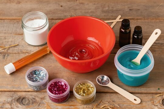 Kids DIY slime making kit with glitter, glue, and other craft supplies on wooden table. Children create sparkly goo, fun sensory play activity.
