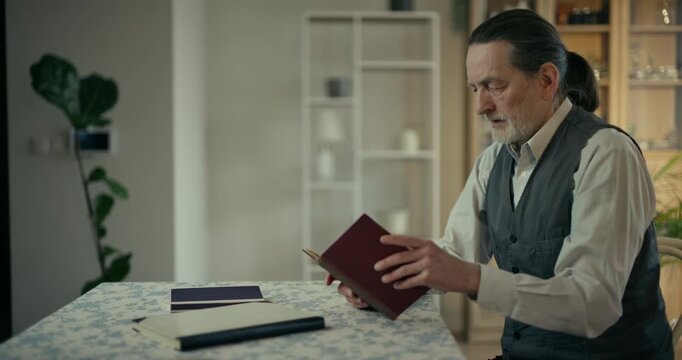 Older man reading a red document at a dining table in a home interior