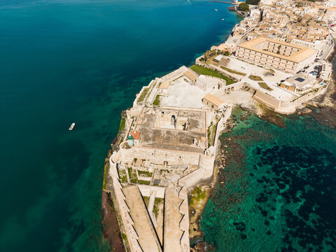Aerial view of the historic Castello Maniace fortress on the tip of Ortygia island with turquoise waters and ancient stone walls in Syracuse, Sicily, Italy.