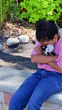 Latina girl hugging her stuffed animal tightly because she is sad.