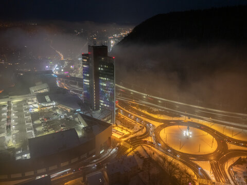 Aerial view of Europa SC and the Europa Business Center skyscraper at night with an illuminated roundabout and fog rolling over the hills in Banska Bystrica, Banskobystricky kraj, Slovakia.