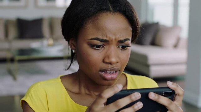 Young Black woman in yellow shirt looking at smartphone with confused expression interior close up