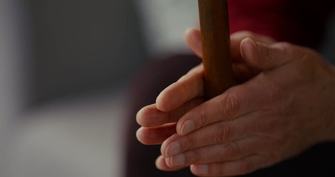 Close-up of adult hands gently gripping a vertical wooden pole indoors