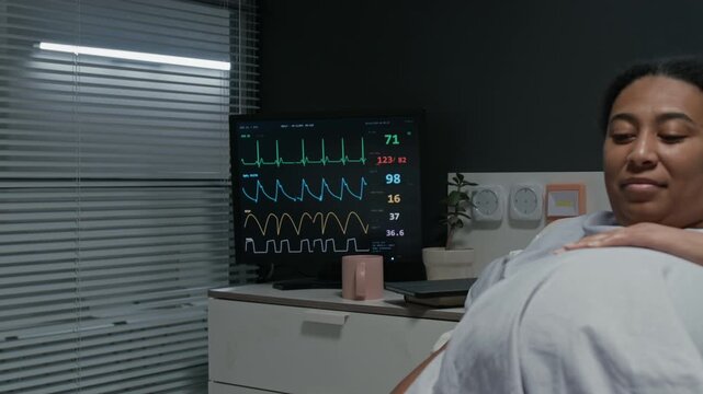 Nurse putting pulse oximeter on pregnant Black woman in hospital bed before walking away. Footage is ideal for maternity care and medical services marketing campaigns, close up