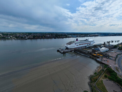 Aerial view of a cruise ship docked at the London International Cruise Terminal on the River Thames with muddy banks and urban skyline in Tilbury, England, United Kingdom.