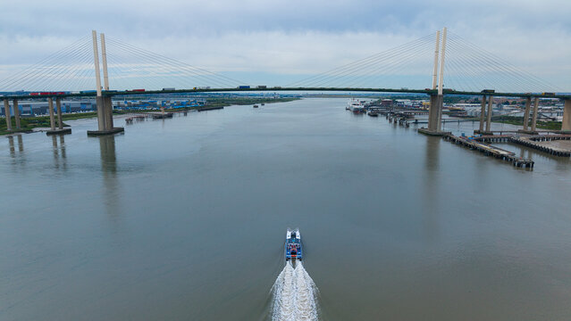 Aerial view of an Uber speedboat cruising on the water towards the Queen Elizabeth II Bridge with industrial docks on the banks in River Thames, Greater London, United Kingdom.